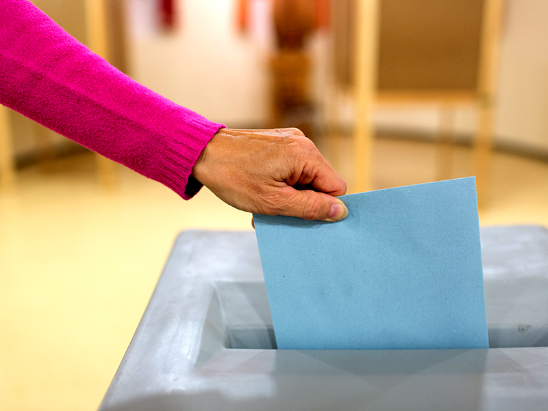 Frau gibt Kuvert in die Wahlurne